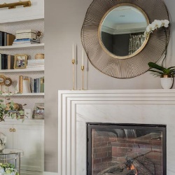 A round brass wire mirror over a white art deco fireplace mantel