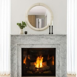 A round ivory shagreen mirror over a marble fireplace mantel